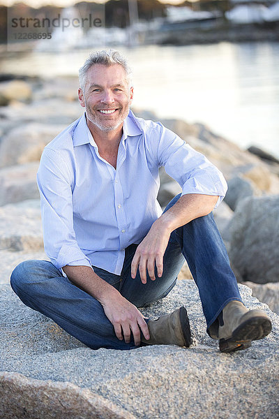 Porträt eines grauhaarigen Mannes  der auf einem Küstenfelsen sitzt und lächelt  Dennis  Massachusetts  USA