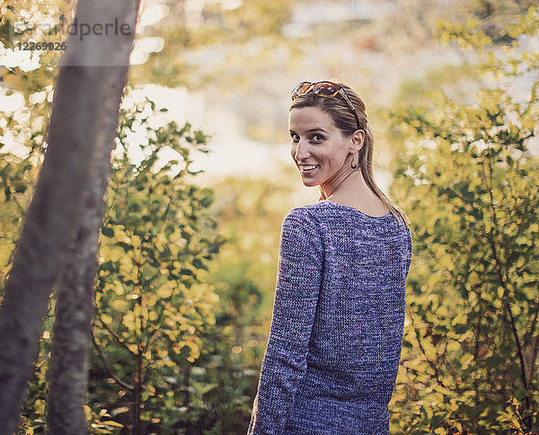 Porträt einer jungen Frau  die im Wald steht und lächelt  während sie über die Schulter schaut  Maine  USA