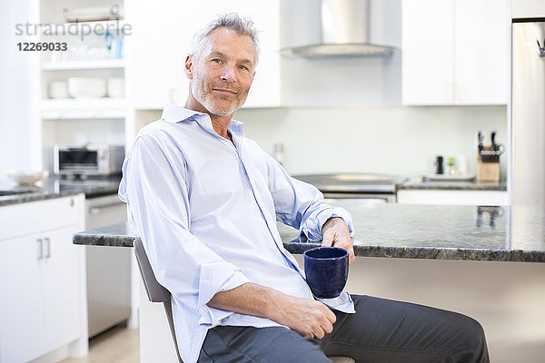 Porträt eines grauhaarigen Mannes  der eine Tasse hält und sich an den Küchentisch lehnt  Massachusetts  USA
