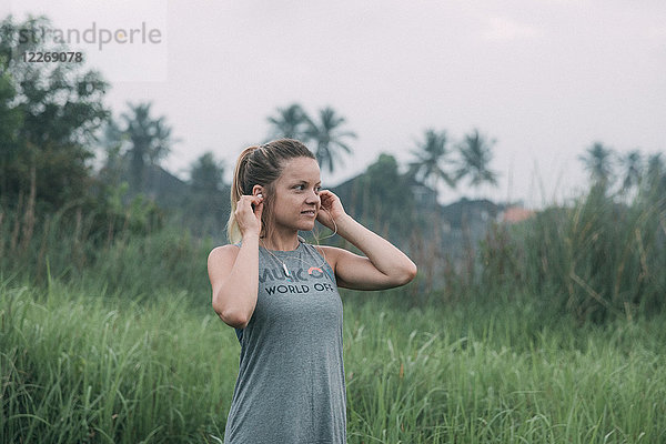 Erwachsene Frau steht im Freien und setzt vor dem Morgenlauf Kopfhörer auf  Bali  Indonesien