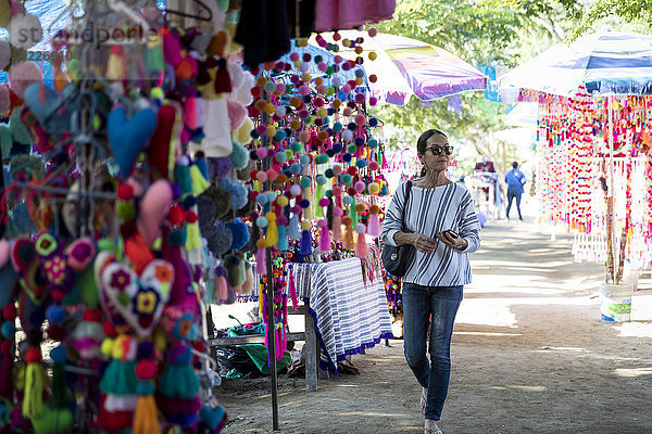 Frau mittleren Alters geht über einen Kunstmarkt und betrachtet bunte Waren  Sayulita  Mexiko