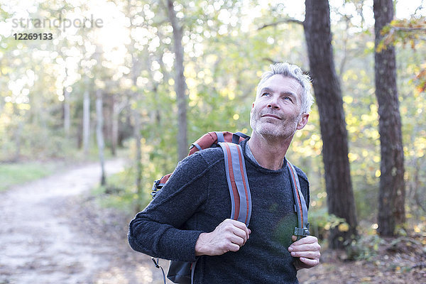 Grauhaariger Mann  der lächelt und aufblickt  während er mit Rucksack im Wald wandert  Massachusetts  USA