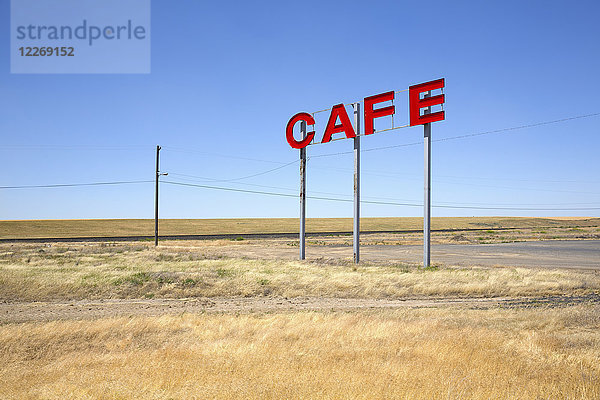 Große rote Großbuchstaben auf Metallstangen  die für ein Café in einer Prärie werben.