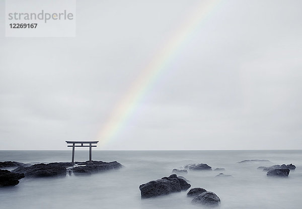Regenbogen über hohem Torii-Tor auf Felsen in der Mitte eines Sees.