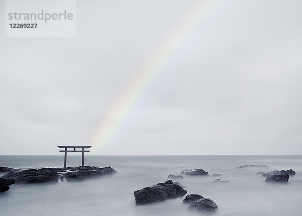 Regenbogen über hohem Torii-Tor auf Felsen in der Mitte eines Sees.
