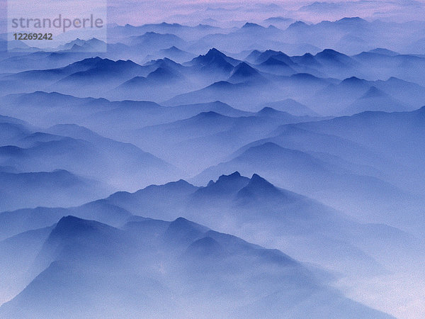 Luftaufnahme eines in der Dämmerung in Nebel gehüllten Gebirges.