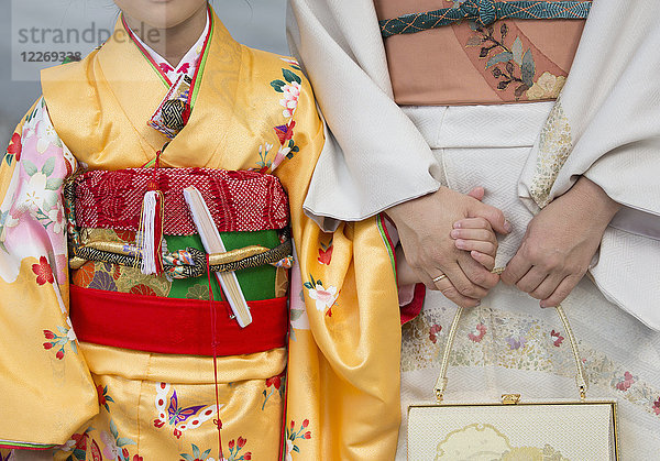 Nahaufnahme einer Frau und eines Kindes  die sich an den Händen halten  in traditionellen japanischen Kimonos nebeneinander stehen und Smartphones halten.