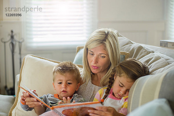 Mittlere erwachsene Frau liest mit Tochter und Kleinkind Sohn auf dem Sofa
