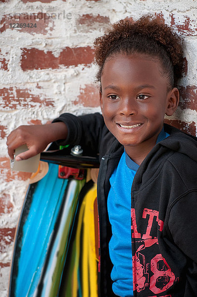 Porträt eines Jungen im Freien  der ein Skateboard hält und lächelt