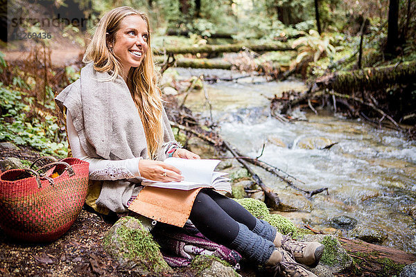 Junge Frau entspannt sich am Waldflussufer mit Notebook