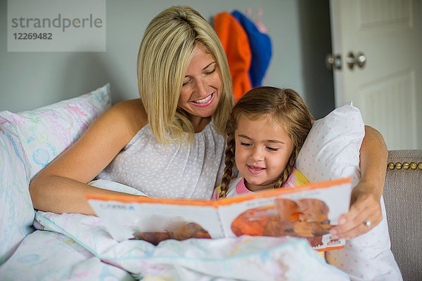 Mittlere erwachsene Frau im Bett mit Tochter  die ein Buch liest