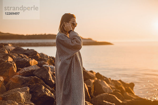 Porträt einer Frau mit Sonnenbrille und Wintermantel auf Felsen stehend und aufs Meer blickend  Odessa  Odeska Oblast  Ukraine  Osteuropa