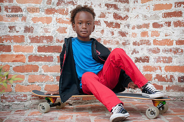 Porträt eines Jungen  der auf einem Skateboard sitzt