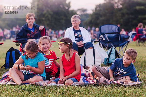 Gruppe von Erwachsenen und Kindern  im Freien sitzend  während der Feierlichkeiten zum 4. Juli