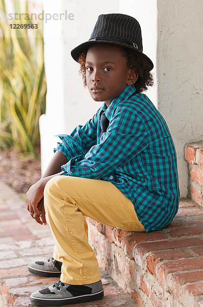 Porträt eines Jungen  der im Freien sitzt und einen Filzhut trägt