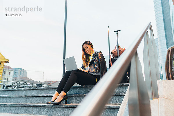 Geschäftsfrau  sitzt im Freien auf einer Treppe  benutzt Laptop  Gepäck neben ihr  niedriger Blickwinkel