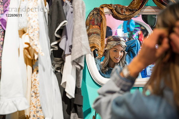 Spiegelbild einer jungen Frau  die im Secondhand-Laden Vintage-Kleidung anprobiert