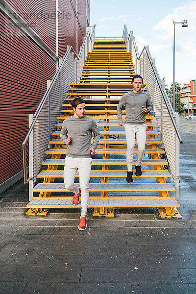 Junge erwachsene männliche Zwillinge laufen zusammen  laufen die Stadttreppe hinunter