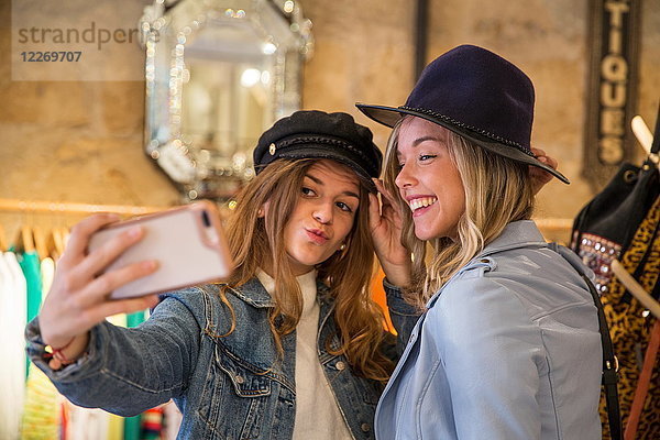 Zwei Freunde im Geschäft  Hüte anprobieren  Selfie nehmen  Smartphone benutzen