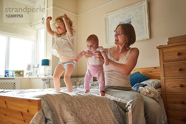 Frau im Bett spielt mit Baby- und Kleinkind-Töchtern