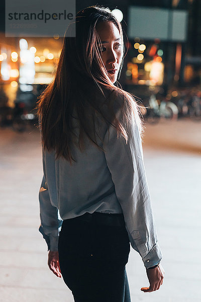 Porträt einer Frau im mittleren Erwachsenenalter  nachts im Freien  über die Schulter schauend