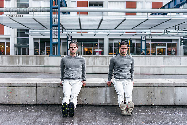 Junge männliche Zwillinge stoßen in der Stadt rückwärts gegen die Wand