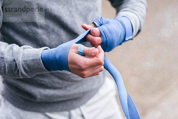 Junger männlicher Boxer trainiert im Freien  bandagiert die Hände mit Handumschlägen  Mittelteil