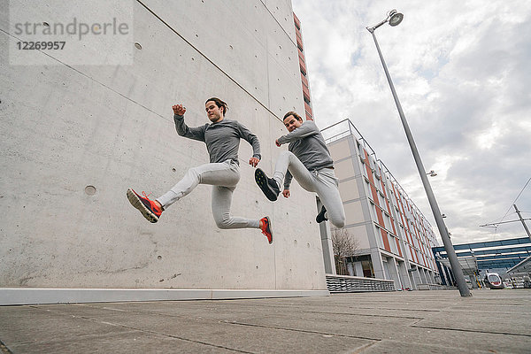 Junge erwachsene männliche Zwillingsläufer  rennen und springen mitten in der Luft auf dem Bürgersteig der Stadt