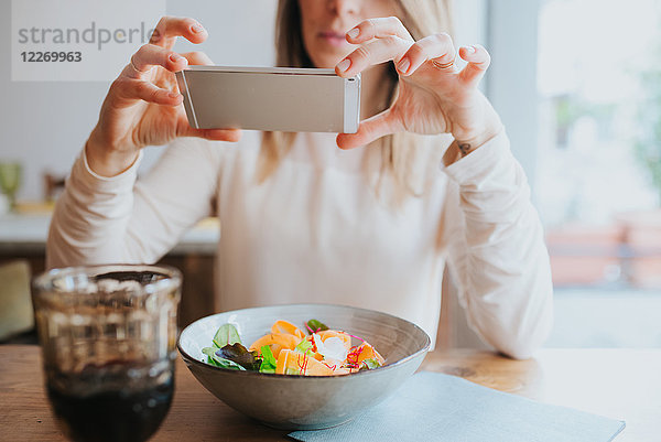 Frau fotografiert veganes Essen im Restaurant