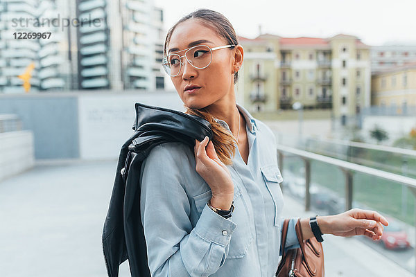 Porträt einer Geschäftsfrau im Freien  Lederjacke über der Schulter tragend  wegschauend  nachdenklicher Ausdruck