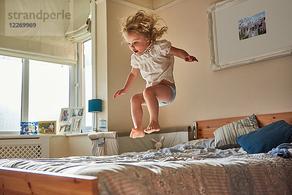 Weibliches Kleinkind springt mitten in der Luft auf dem Bett