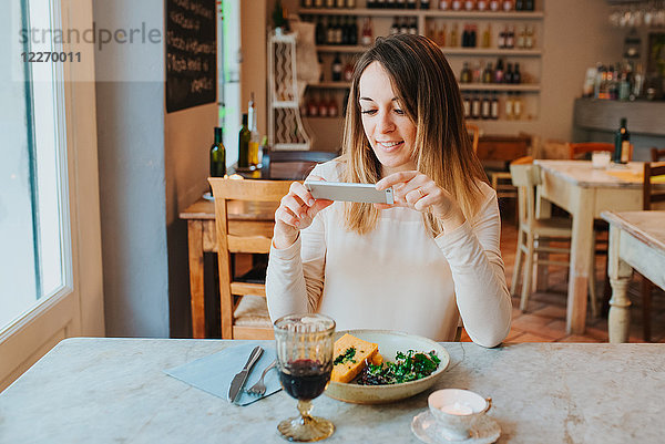 Frau fotografiert veganes Essen im Restaurant