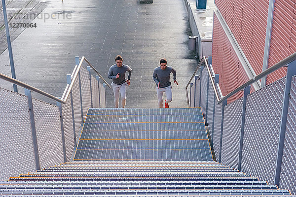 Junge erwachsene männliche Zwillinge laufen zusammen und laufen die Stadttreppe hinauf