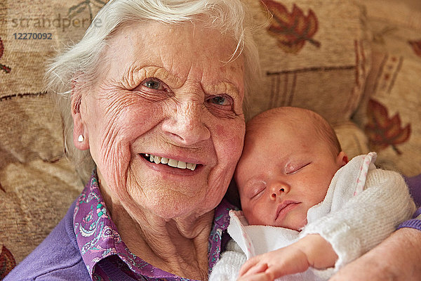 Ältere Frau wiegt Baby Urenkelin auf Sessel  Portrait