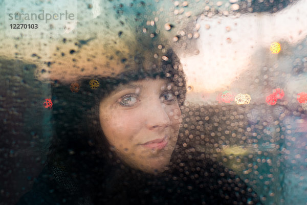 Frau schaut aus dem regennassen Fenster