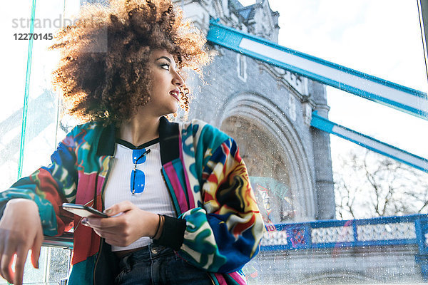Junges Mädchen im Freien  hält Smartphone in der Hand  schaut weg  Tower Bridge im Hintergrund  London  England  UK