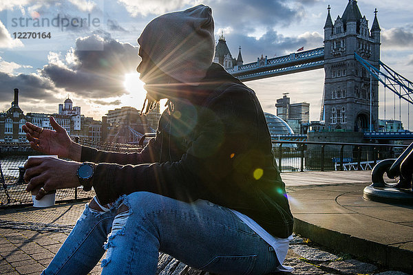 Junger Mann sitzt im Freien  hält Kaffeetasse  Tower Bridge  London  England  UK