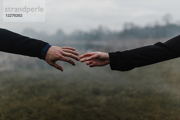 Schrägansicht eines jungen Paares  das Hände hält und sich mit den Fingern berührt