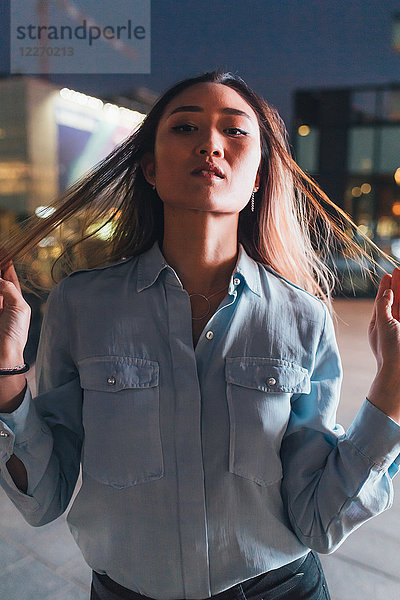 Porträt einer Frau im mittleren Erwachsenenalter  nachts im Freien  Haare zwischen den Fingern ziehen  ernster Ausdruck
