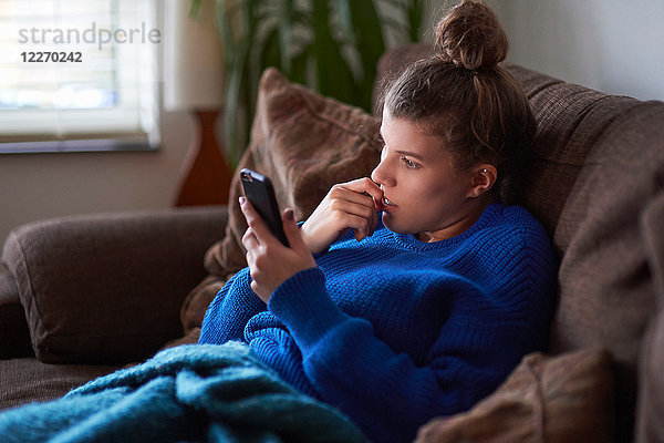 Junge Frau auf Sofa schaut auf Smartphone