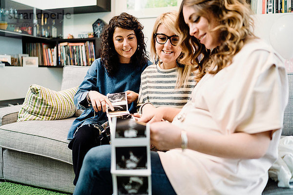 Schwangere und Freundinnen auf dem Sofa beim Betrachten von Ultraschallbildern