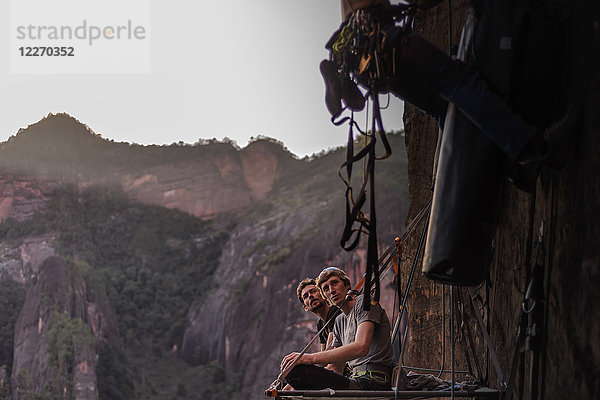 Zwei Felskletterer sitzen auf dem Portalege und beobachten  wie ein Freund neben ihnen klettert  Liming  Provinz Yunnan  China
