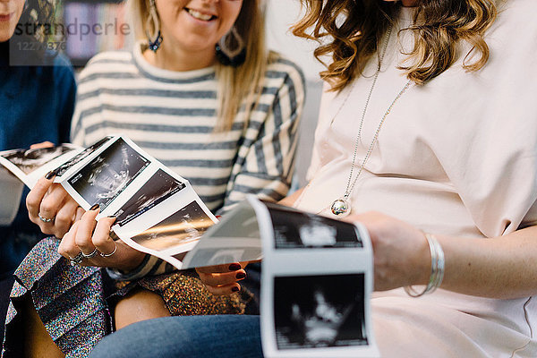 Schwangere und Freundinnen auf dem Sofa beim Betrachten von Ultraschallbildern  ausgeschnitten