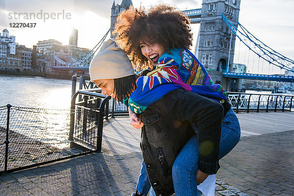 Junge gebende junge Frau huckepack im Freien  Tower Bridge im Hintergrund  London  England  UK