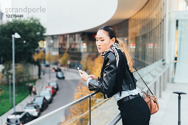 Frau  im Freien  an Geländer gelehnt  Smartphone halten