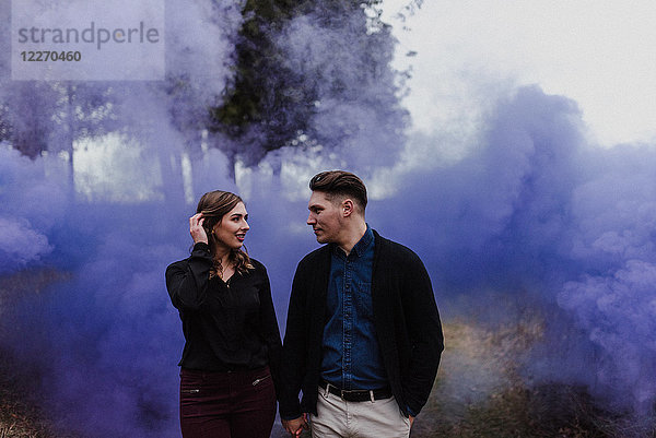 Junges Paar hält sich an blauer Rauchwolke an den Händen