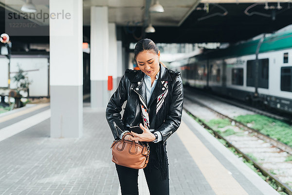 Frau geht am Bahnsteig entlang  durchsucht Tasche  benutzt Smartphone