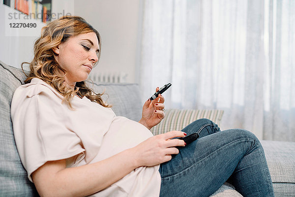 Schwangere Frau auf dem Sofa betrachtet Blutzuckertestergebnis