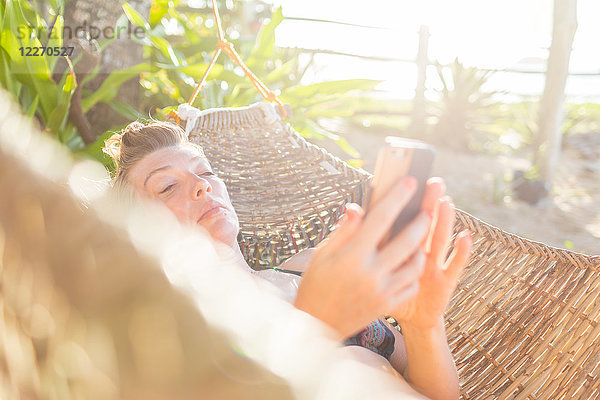 Frau entspannt sich auf Hängematte  mit Smartphone  Nacpan Beach  Palawan  Philippinen