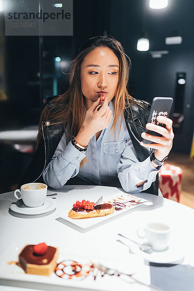 Frau sitzt im Restaurant  isst Nachtisch  benutzt Smartphone
